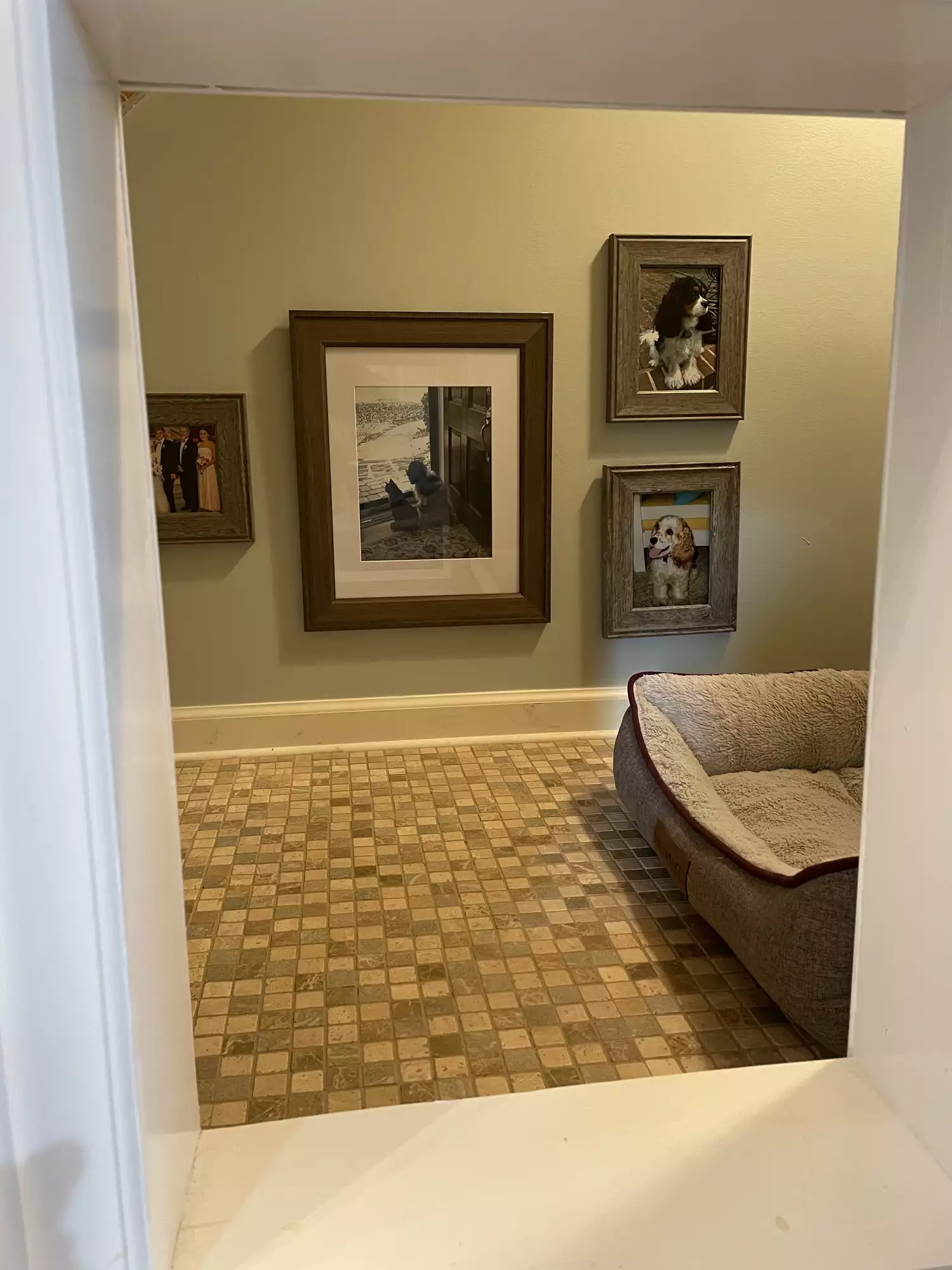 The inside of a pet nook. Light green walls and a tile floor. There are framed pictures and a dog bed.